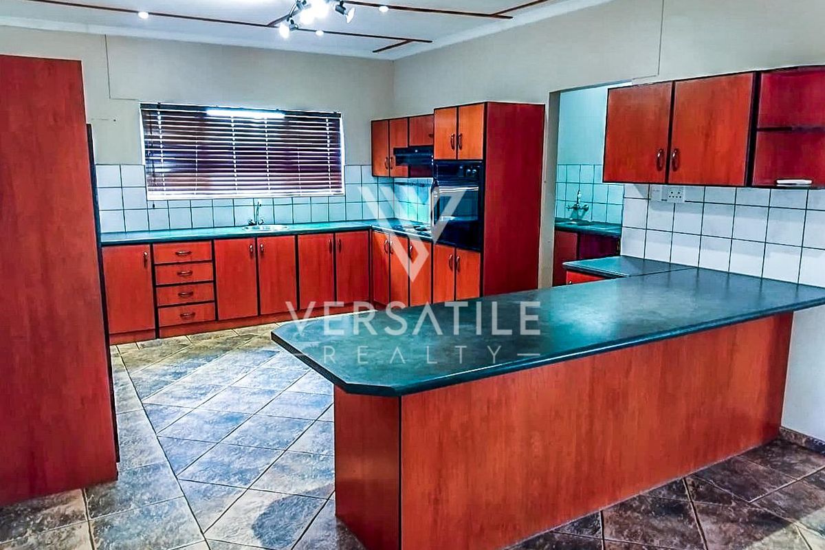 Spacious kitchen featuring wooden cabinetry, dark laminate countertops, tiled flooring, and a built-in oven with an integrated hob.