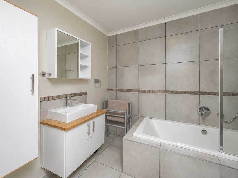A modern, well-maintained bathroom featuring a vessel sink vanity, built-in bathtub with a glass shower screen, and neutral large-format wall and floor tiles.