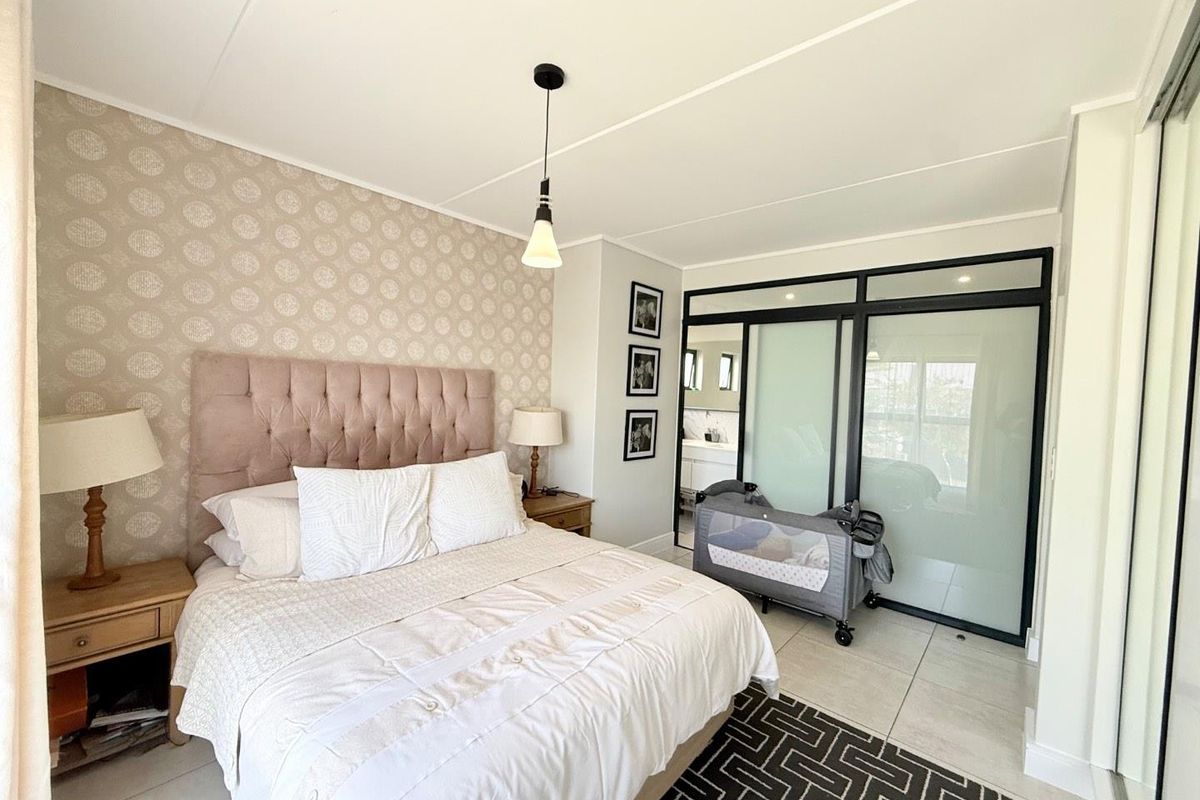 A well-maintained bedroom featuring patterned wallpaper, tiled flooring, and a modern black-framed glass partition leading to an en-suite bathroom.