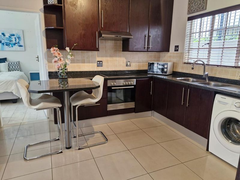 A functional kitchen featuring dark wood cabinetry, granite countertops, built-in oven, hob, extractor fan, and integrated laundry appliance space.