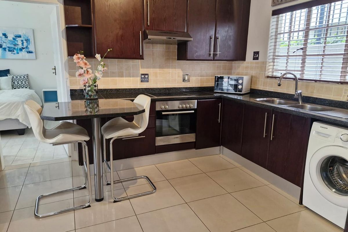 A functional kitchen featuring dark wood cabinetry, granite countertops, built-in oven, hob, extractor fan, and integrated laundry appliance space.