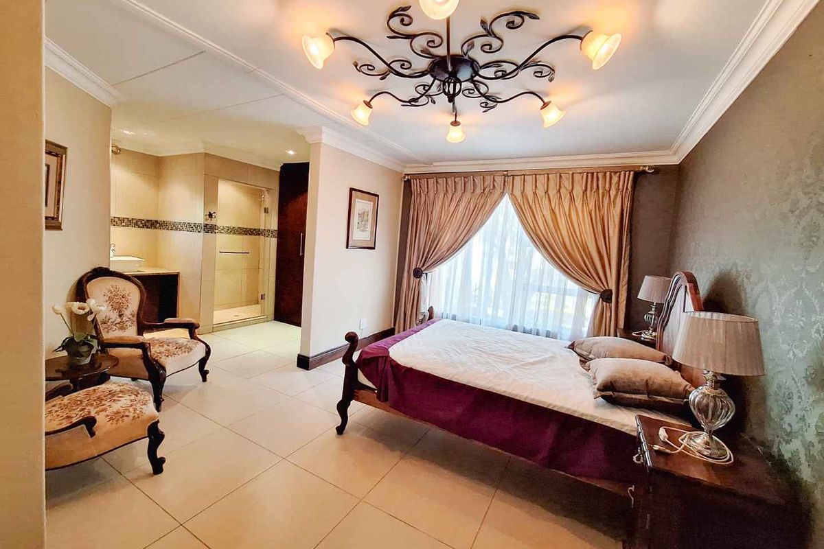 Spacious bedroom featuring tiled flooring, crown molding, a decorative chandelier, and an integrated en-suite bathroom with a glass-enclosed shower.