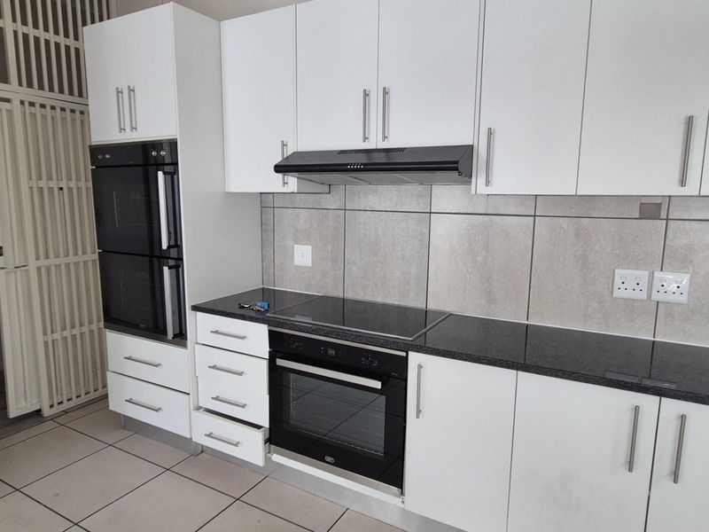 Modern kitchen featuring white cabinetry, granite countertops, built-in oven, electric hob, and extractor fan, complemented by neutral tiled flooring and splashbacks.