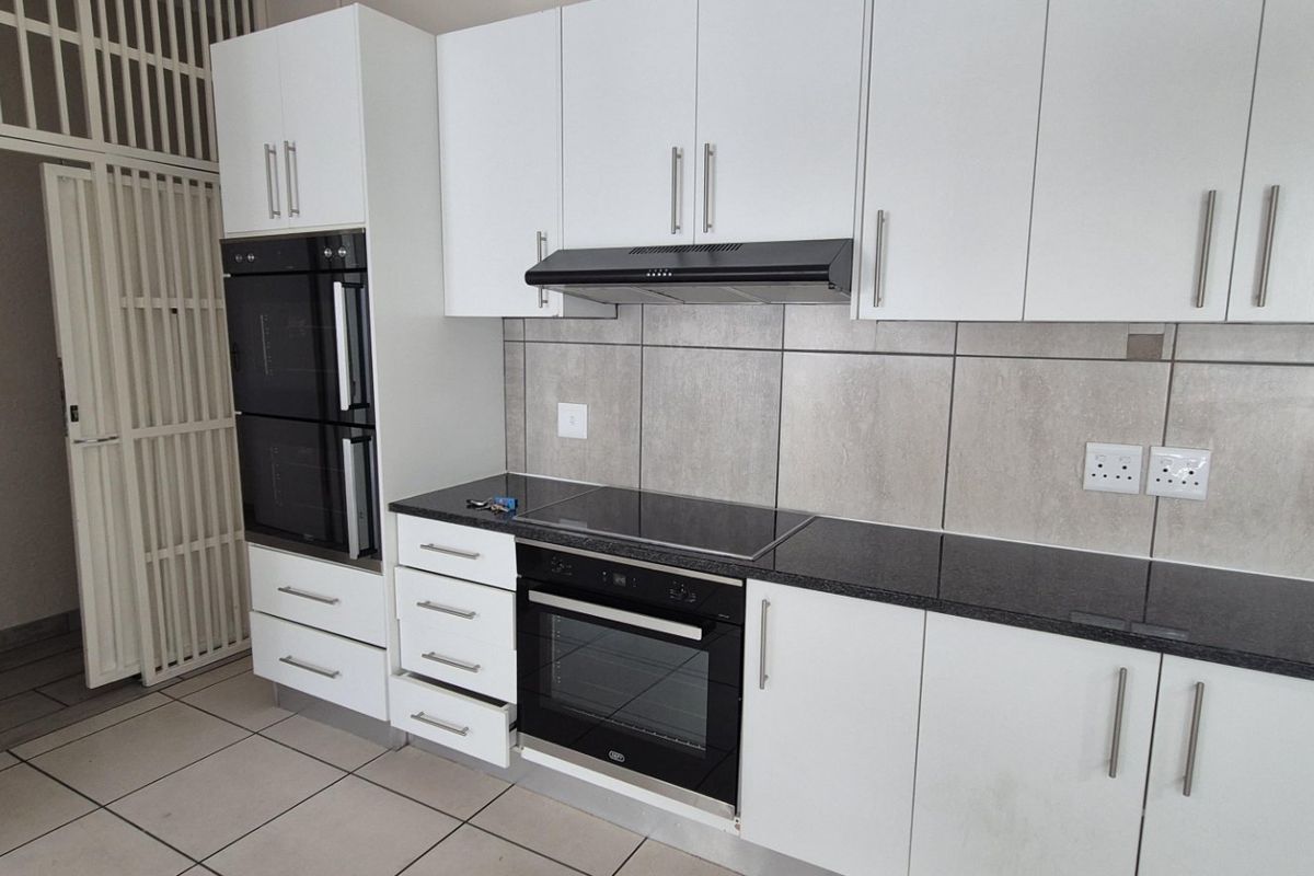 Modern kitchen featuring white cabinetry, granite countertops, built-in oven, electric hob, and extractor fan, complemented by neutral tiled flooring and splashbacks.