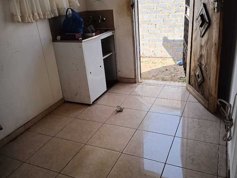 A functional scullery or utility area featuring tiled flooring, a sink cabinet, and direct access to the exterior through a timber door.