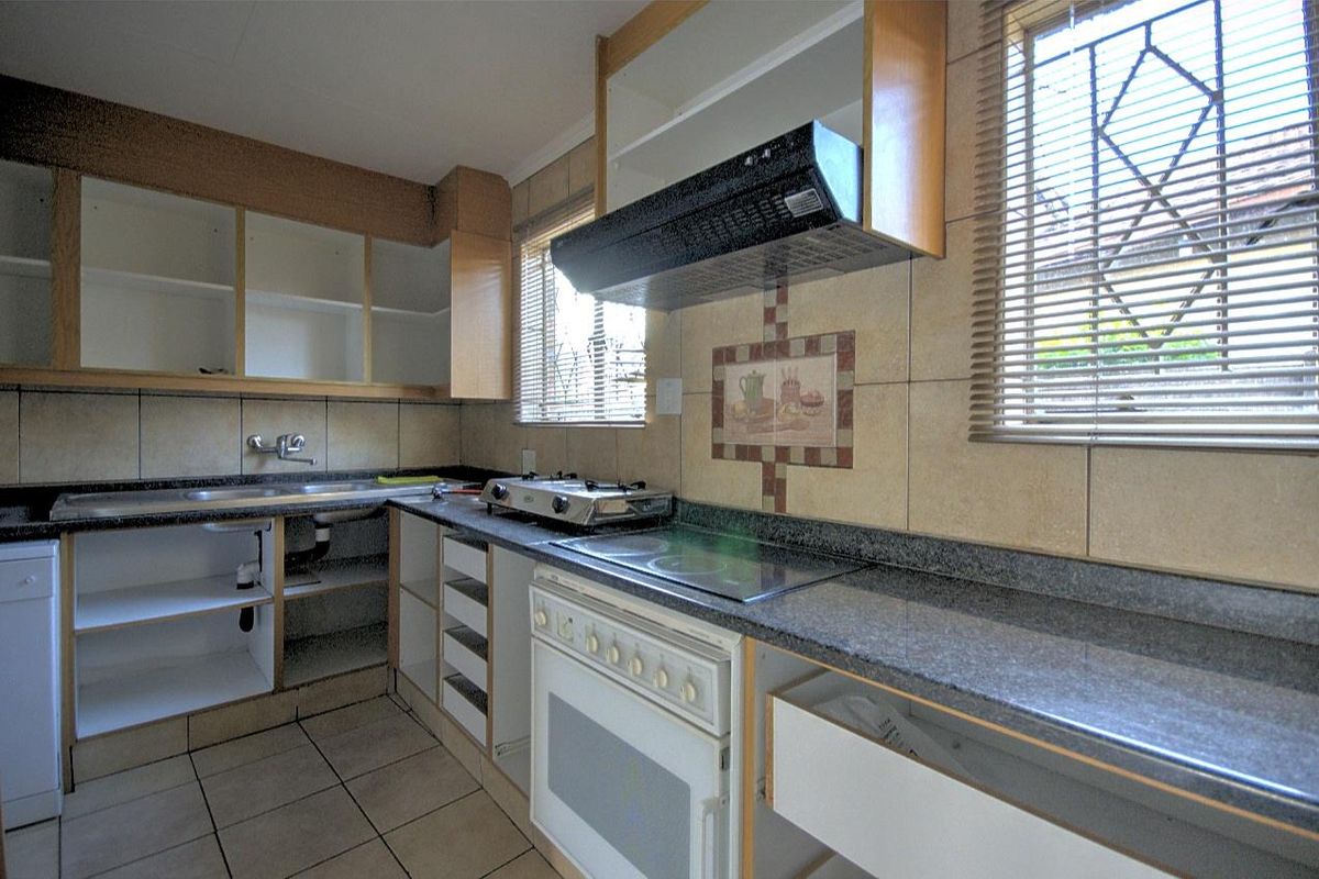 A dated kitchen featuring granite countertops, a built-in oven and hob, extractor fan, and tiled flooring, currently requiring cabinet repairs and cosmetic updates.