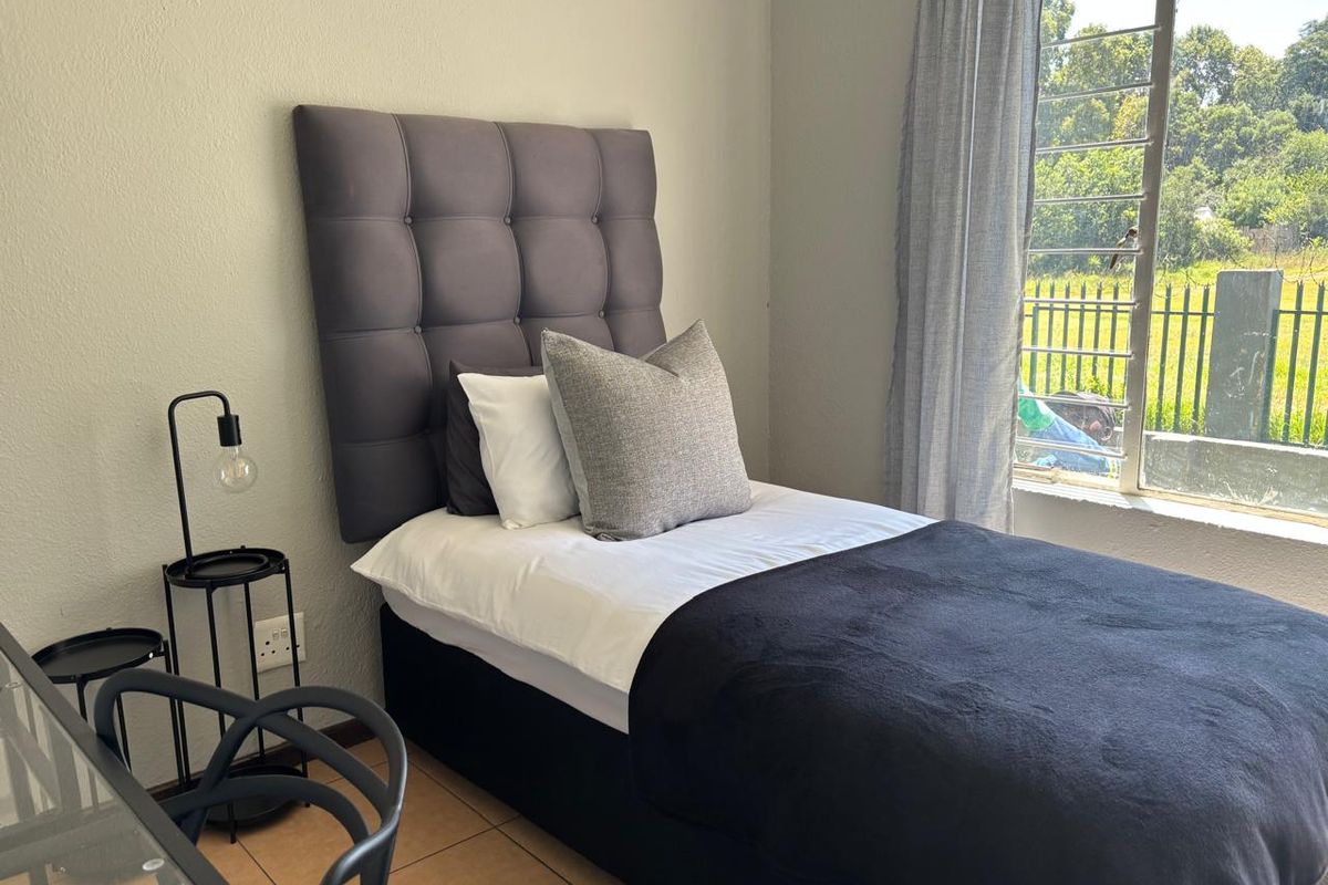 A bedroom featuring tiled flooring and a window with security bars, offering natural light and a view of the exterior surroundings.