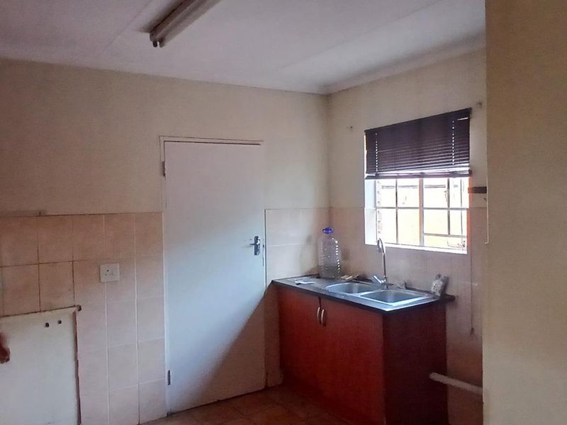 A dated kitchen area featuring built-in cabinetry, a double sink, and tiled splashbacks, requiring cosmetic updates to modernize the space.