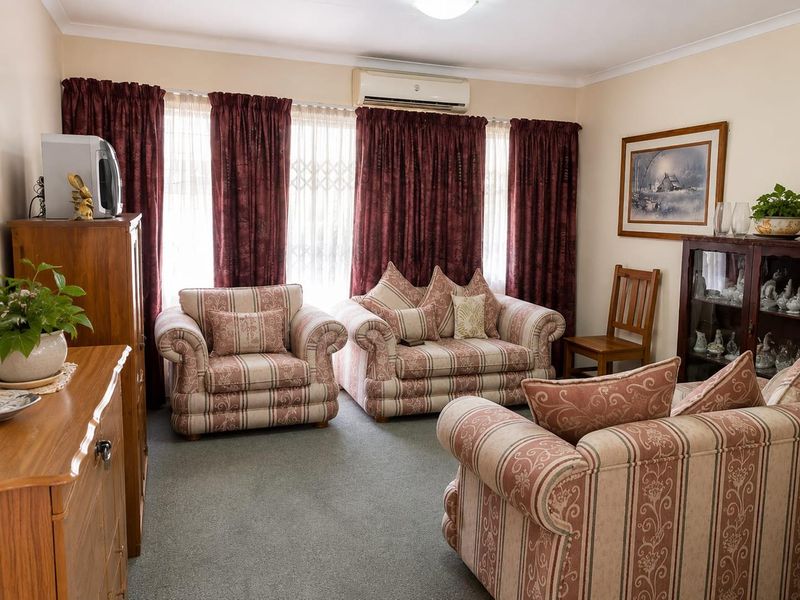A comfortable living room featuring carpeted flooring, coving, and a wall-mounted air conditioning unit, providing a functional and well-maintained space.