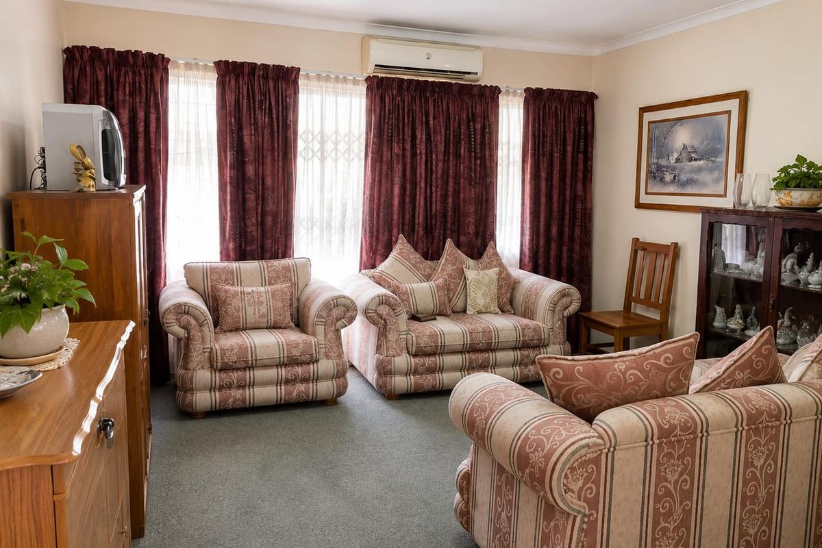 A comfortable living room featuring carpeted flooring, coving, and a wall-mounted air conditioning unit, providing a functional and well-maintained space.