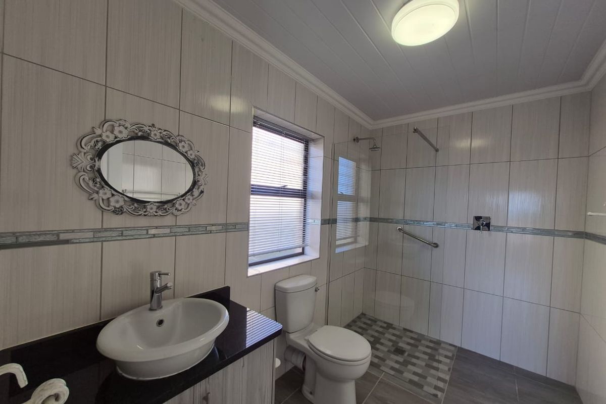 Modern bathroom featuring a vanity with vessel sink, a walk-in shower with glass screen, and neutral floor-to-ceiling wall tiling.