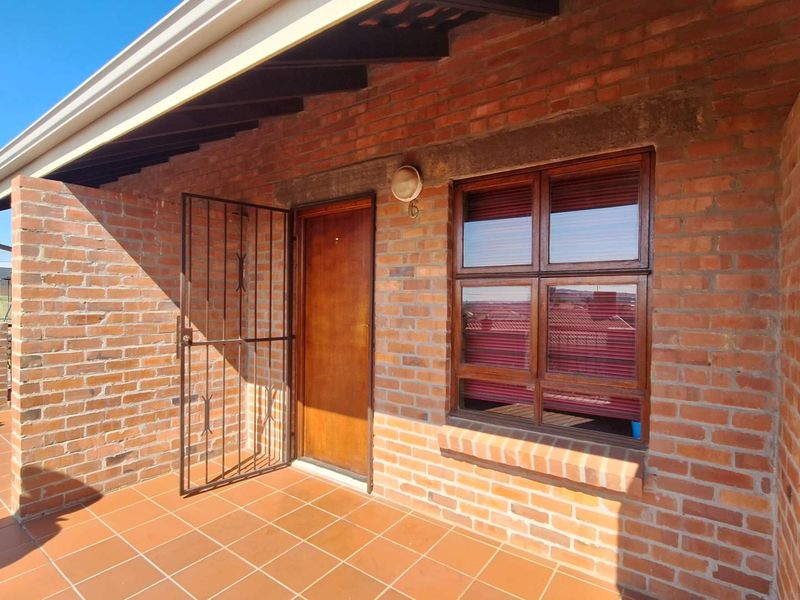 A covered patio area featuring exposed brick walls, tiled flooring, and a secure entrance with a timber door and security gate.