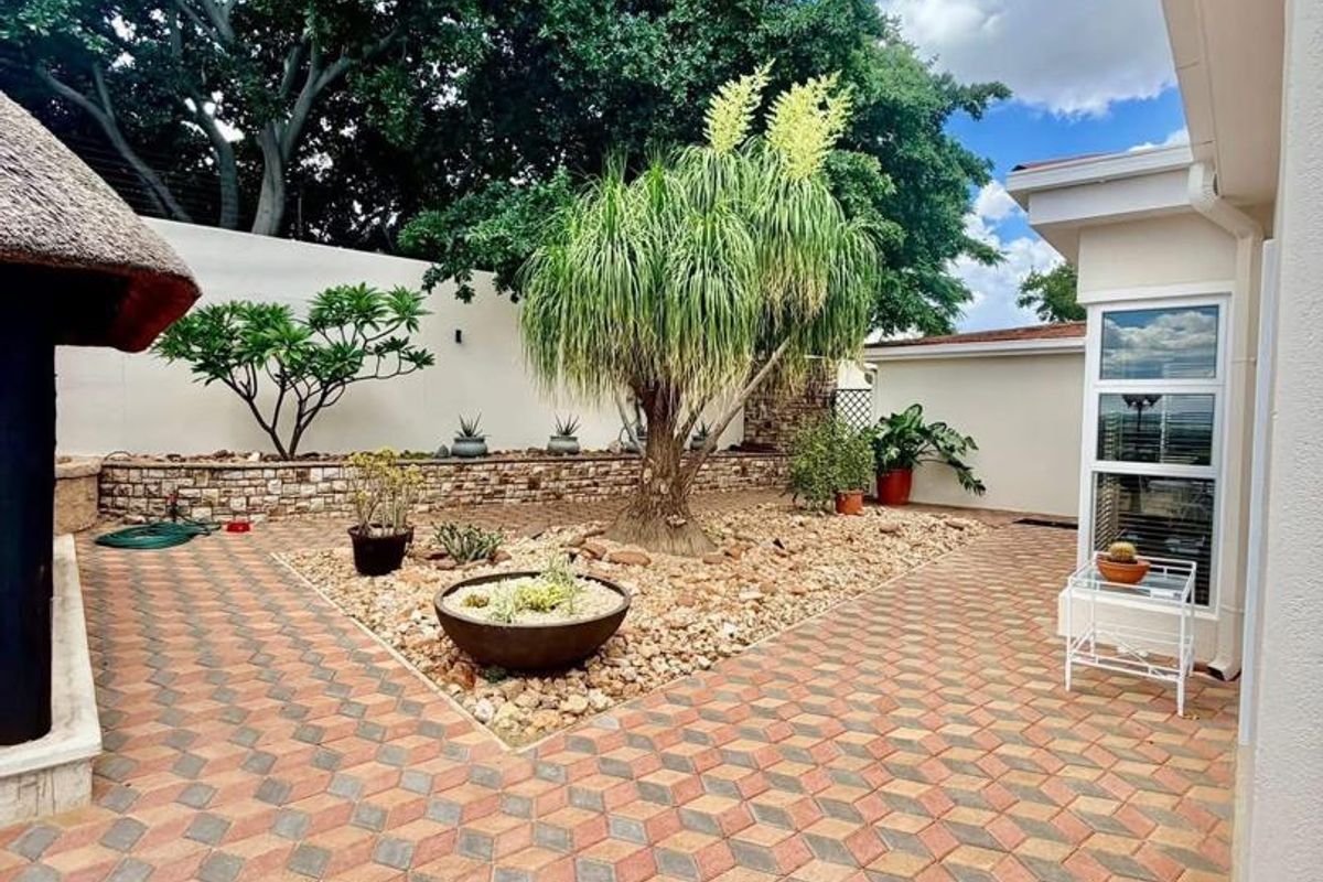 A well-maintained paved courtyard featuring a central landscaped garden bed with a mature ponytail palm and stone retaining wall.