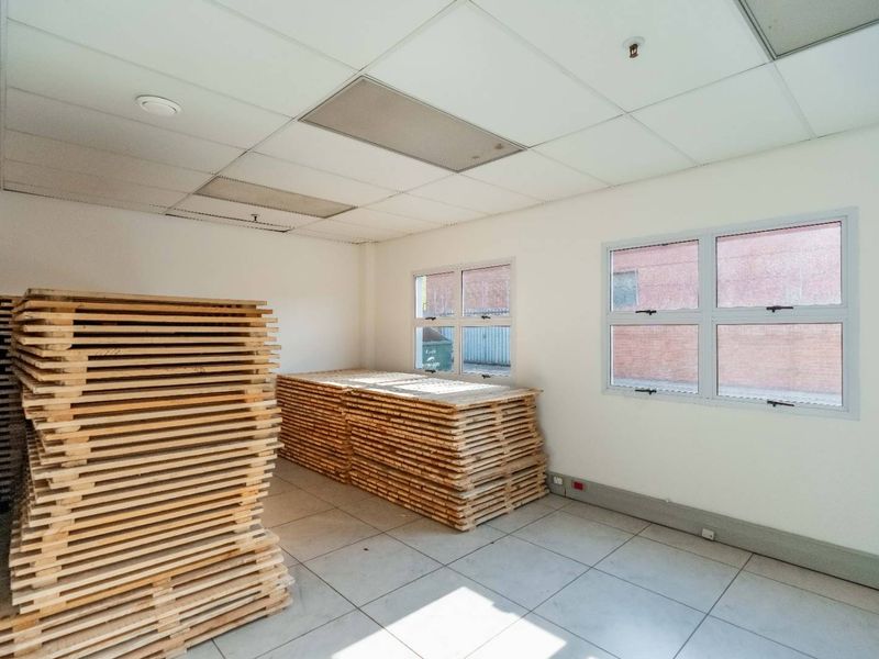 A functional utility space featuring tiled flooring, suspended ceiling tiles, and aluminium-framed windows, suitable for storage or office use.