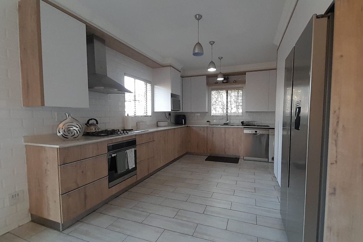 Modern kitchen featuring light wood-grain cabinetry, white countertops, built-in oven, gas hob, stainless steel extractor fan, and tiled flooring.