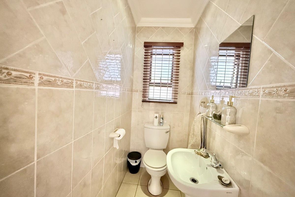 A compact guest bathroom featuring floor-to-ceiling neutral wall tiles, a pedestal basin, and a toilet.
