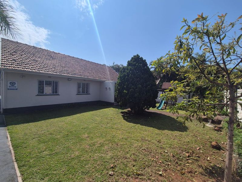 A view of the rear exterior of the house featuring a lawn, mature trees, and a tiled roof.