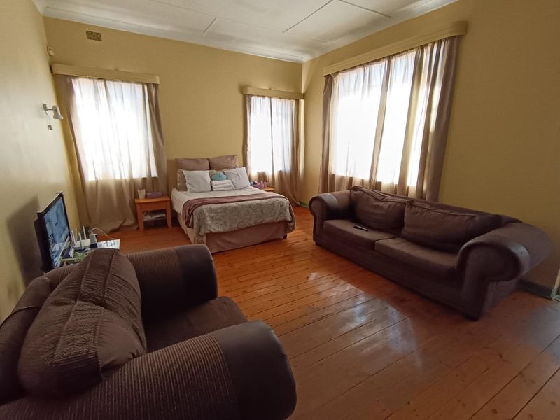 Spacious bedroom featuring original hardwood flooring, high ceilings with cornice detailing, and multiple windows providing natural light.