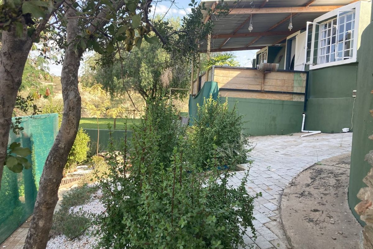 Rear exterior view featuring a covered patio area with timber balustrades, paved walkway, and established garden surroundings.