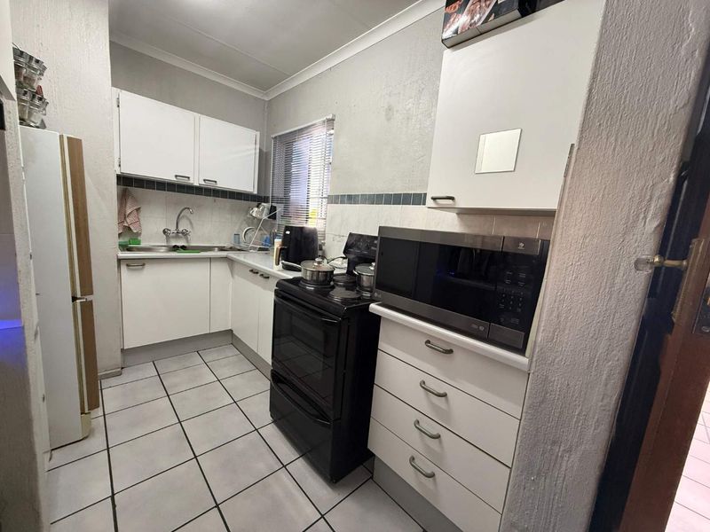 A functional kitchen featuring white cabinetry, tiled flooring, a tiled backsplash, and a freestanding stove, offering a practical layout for daily meal preparation.