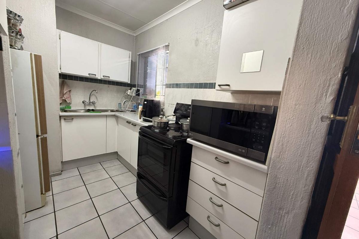 A functional kitchen featuring white cabinetry, tiled flooring, a tiled backsplash, and a freestanding stove, offering a practical layout for daily meal preparation.