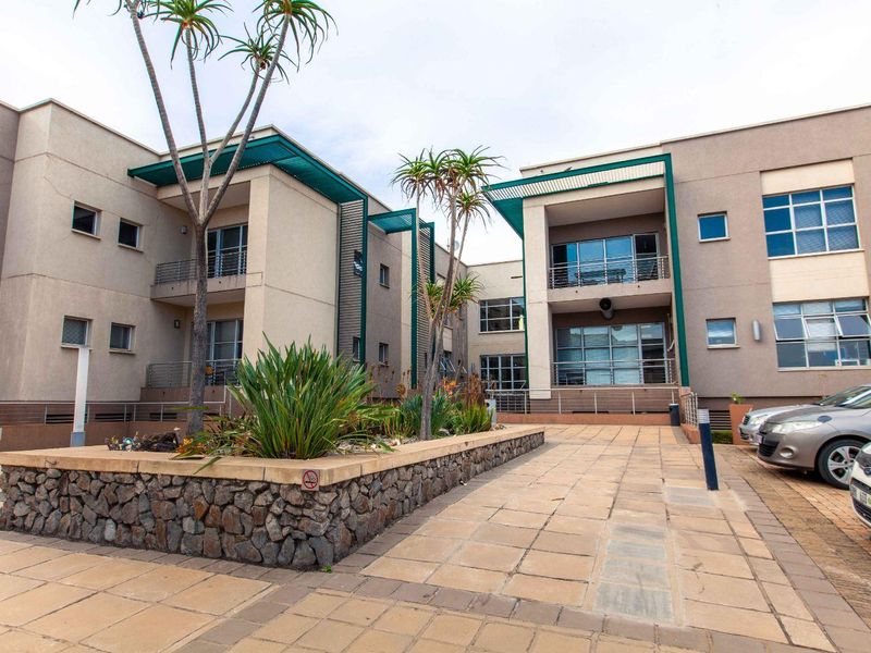 A well-maintained office building exterior featuring a paved courtyard, stone-clad planters, and multi-level balconies with metal railings.