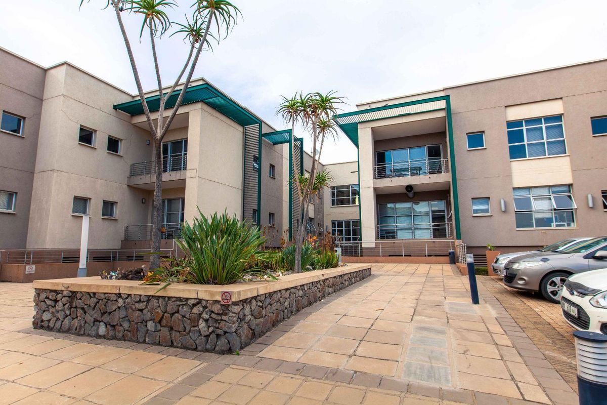A well-maintained office building exterior featuring a paved courtyard, stone-clad planters, and multi-level balconies with metal railings.