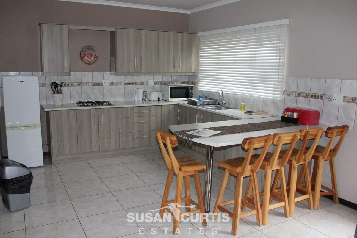 A functional kitchen featuring light wood-grain cabinetry, tiled backsplash, integrated gas hob, and a breakfast bar with tiled flooring.