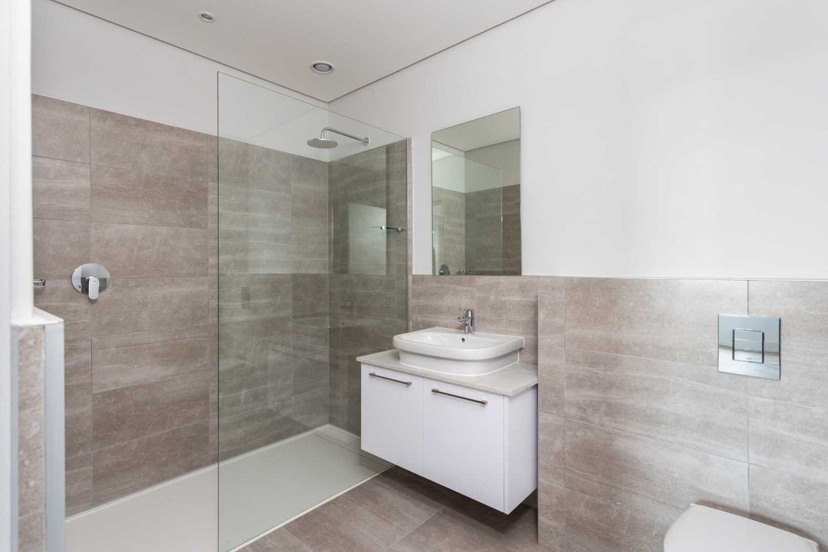 Modern bathroom featuring a walk-in glass shower, wall-mounted vanity with basin, and neutral floor-to-ceiling tiling.