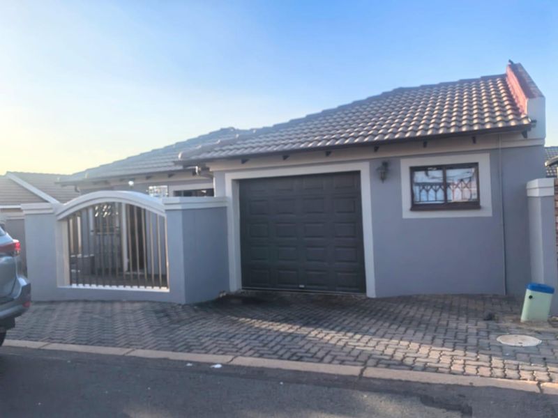 Front elevation of a single-story house featuring a paved driveway, integrated garage, and a secure boundary wall with metal gate.