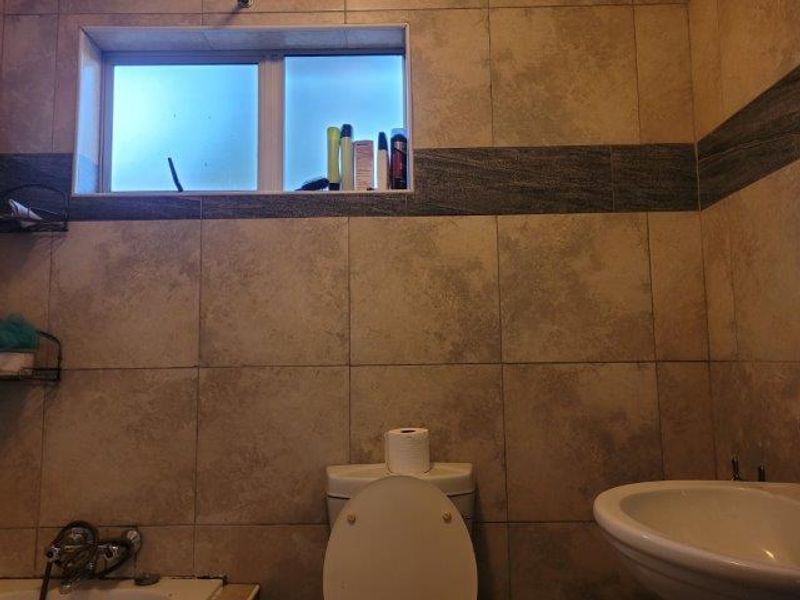 A functional bathroom featuring ceramic wall tiling, a built-in bathtub, a pedestal basin, and a toilet with a frosted glass window.