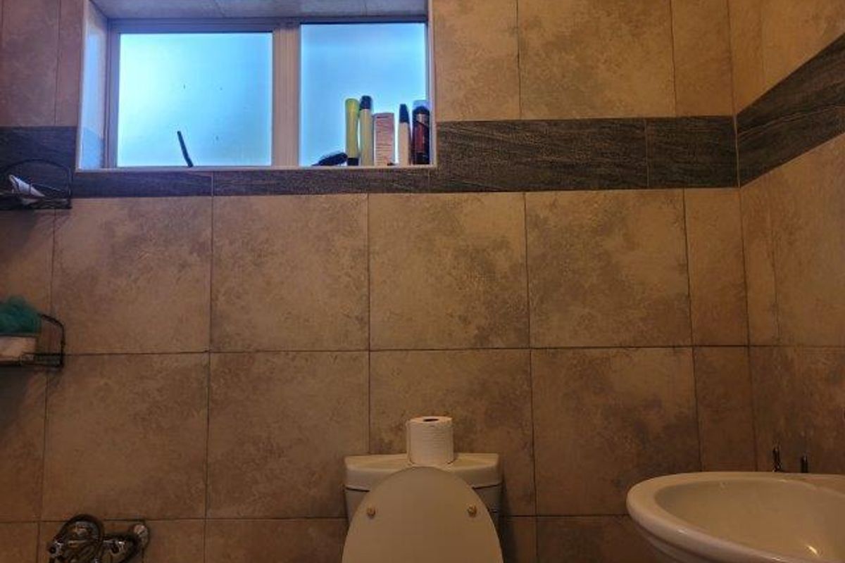 A functional bathroom featuring ceramic wall tiling, a built-in bathtub, a pedestal basin, and a toilet with a frosted glass window.