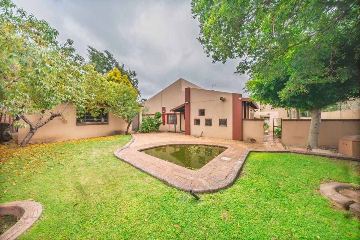 Rear garden area featuring a small built-in pond, paved patio space, and established trees set against the rear elevation of the house.