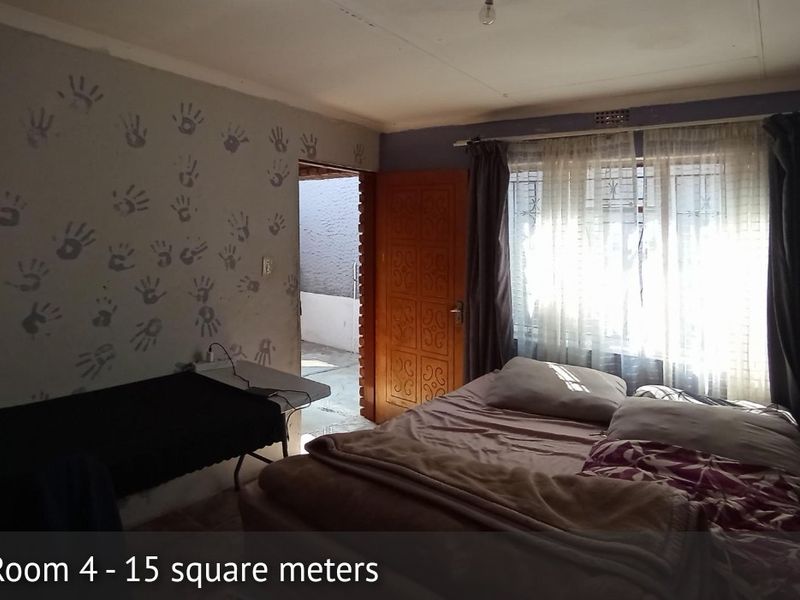 A bedroom featuring a timber door, security gate, and window with burglar bars. The room requires cosmetic updates to the wall finishes.