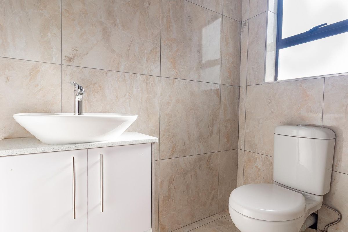 A modern bathroom featuring floor-to-ceiling marble-look wall tiles, a contemporary vessel sink vanity, and a white toilet.