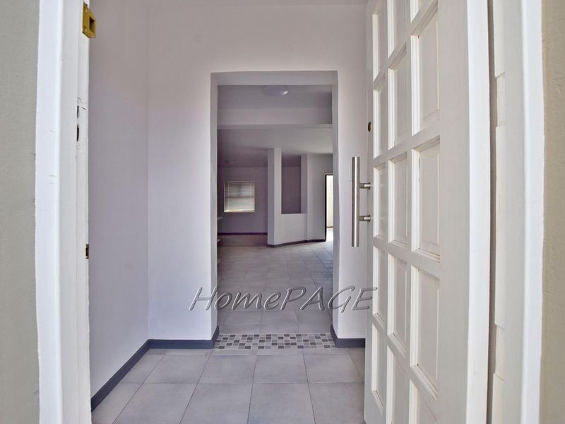 A bright and spacious entrance hall featuring neutral tiled flooring and a classic panelled front door, leading into an open-plan living area.