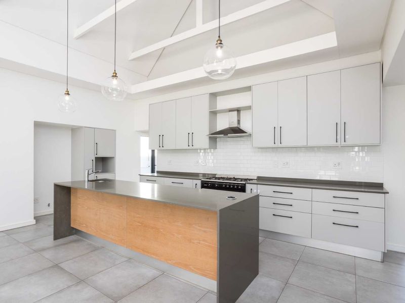 Modern kitchen featuring a large island with stone countertops, gas stove, subway tile backsplash, and vaulted ceilings with exposed rafters.