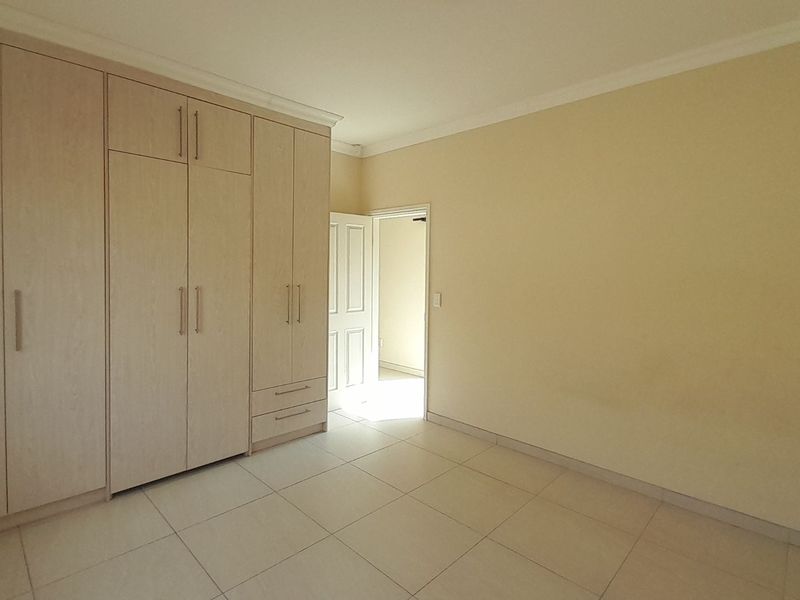 A bright, empty bedroom featuring neutral tiled flooring and extensive built-in wooden cupboards providing ample storage space.