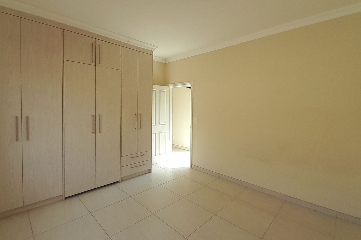 A bright, empty bedroom featuring neutral tiled flooring and extensive built-in wooden cupboards providing ample storage space.