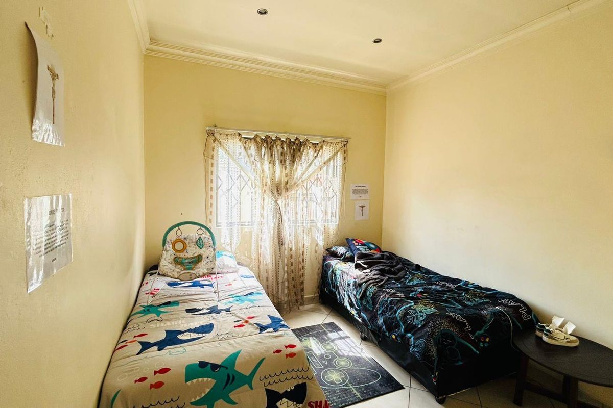 A functional bedroom featuring tiled flooring, recessed ceiling lighting, and security bars on the window.