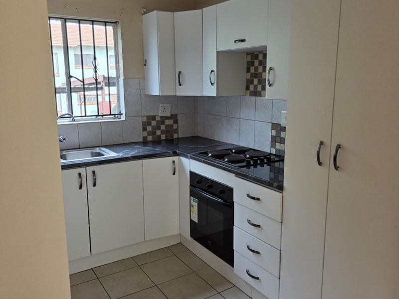 Compact kitchen featuring white cabinetry, dark laminate countertops, built-in oven and hob, tiled backsplash, and tiled flooring.