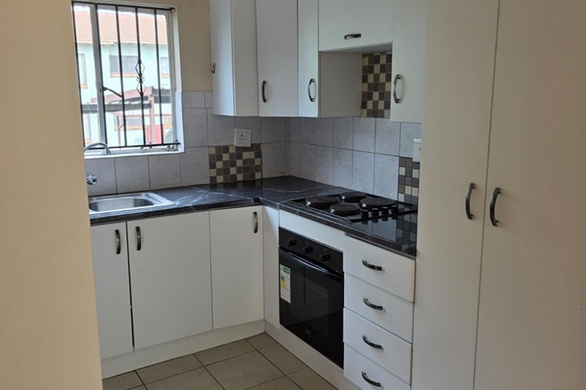 Compact kitchen featuring white cabinetry, dark laminate countertops, built-in oven and hob, tiled backsplash, and tiled flooring.