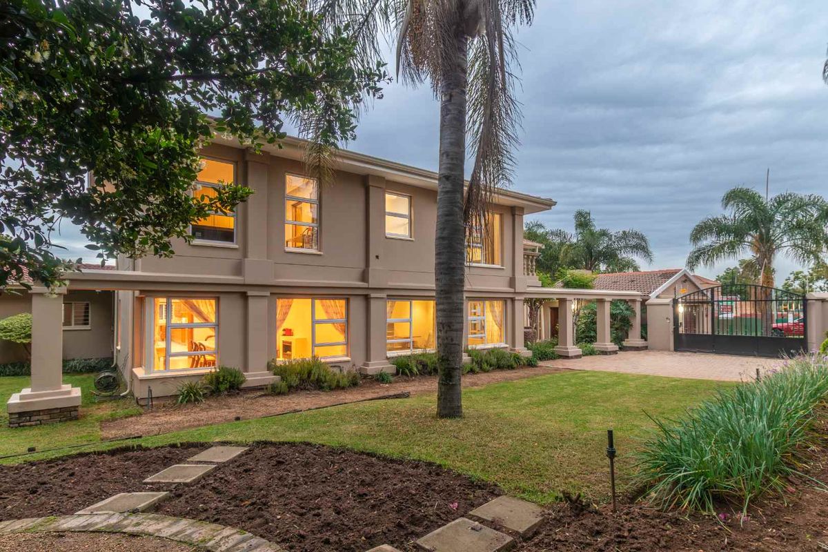 A view of the rear exterior of the two-story house, featuring a landscaped garden, paved driveway, and secure gated entrance.