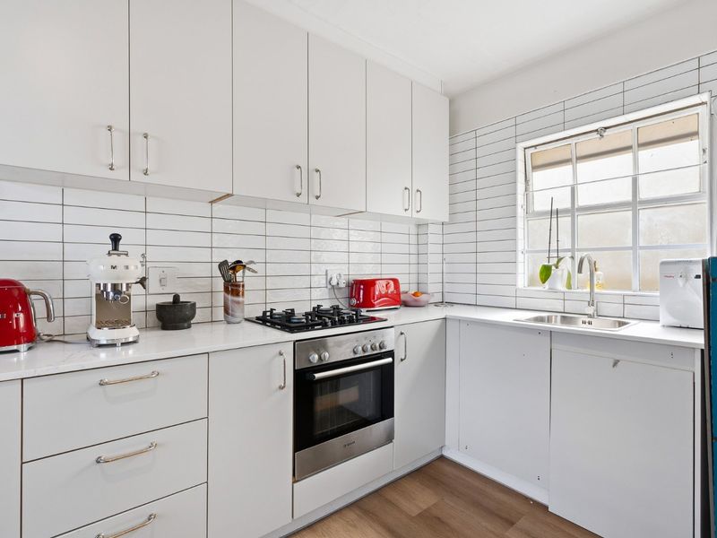 A clean, functional kitchen featuring white cabinetry, subway tile backsplash, a gas cooktop, built-in oven, and a stainless steel sink.