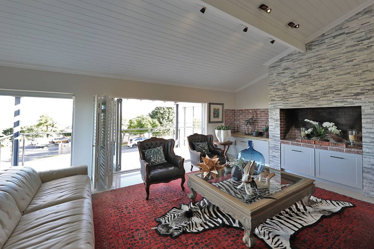 Spacious living room featuring a vaulted tongue-and-groove ceiling, a striking stone-clad fireplace, and large bi-fold doors opening to a balcony with scenic views.