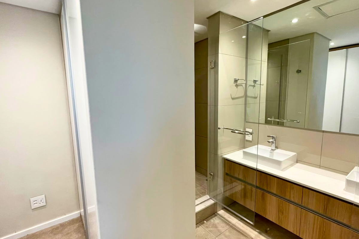 Modern bathroom featuring a sleek double vanity with vessel sinks, large wall mirror, and a glass-enclosed shower area with neutral tiling.