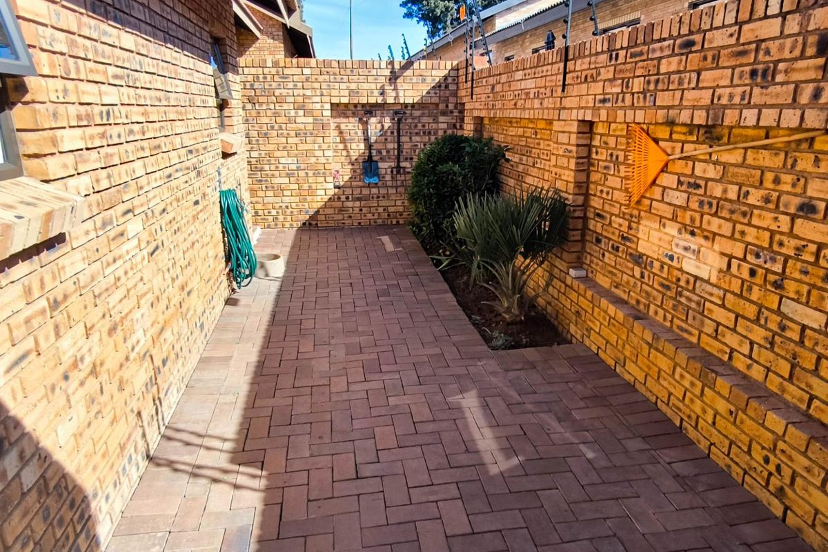 A paved side courtyard featuring face-brick walls, integrated security fencing, and a small landscaped garden bed.