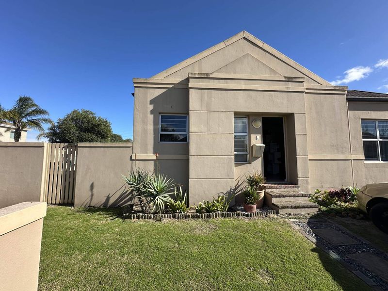 Front elevation of a townhouse featuring a gabled roof, plastered exterior walls, and a small private garden with a paved entrance path.