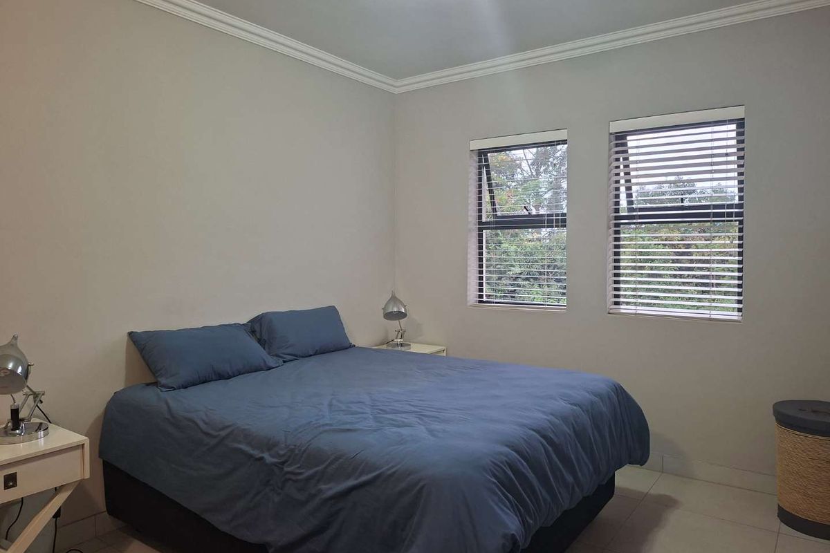 A well-lit bedroom featuring neutral wall tones, tiled flooring, and dual windows fitted with horizontal blinds.