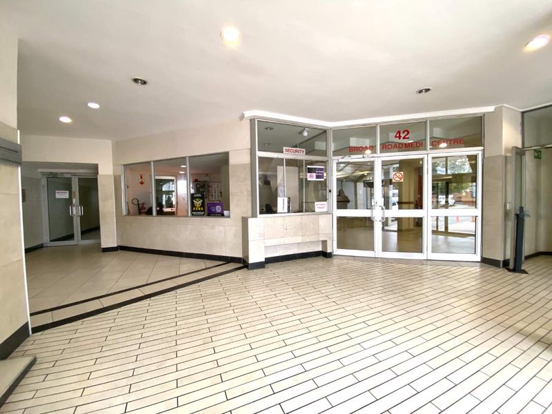 A bright and spacious building entrance lobby featuring tiled flooring, a dedicated security office, and glass-paneled double entrance doors.